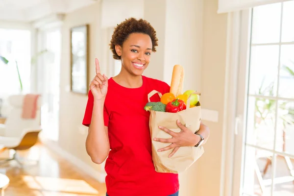 若いアフリカ系アメリカ人女性持株紙新鮮な食料品アイデアに驚きの完全をバッグや幸せそうな顔 ナンバーワンと人差し指の質問 — ストック写真