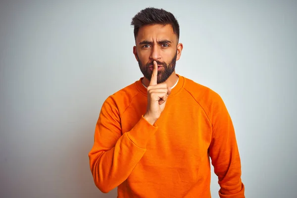 孤立した白い背景の上にオレンジ色のセーターを着た若いインド人男性が 唇に指で静かにするように頼んだ 沈黙と秘密の概念 — ストック写真