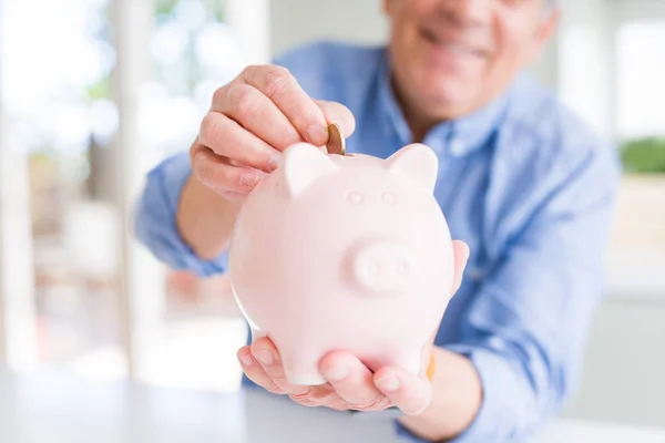 Man putting a coin inside piggy bank as savings smiling confiden — Stock Photo, Image