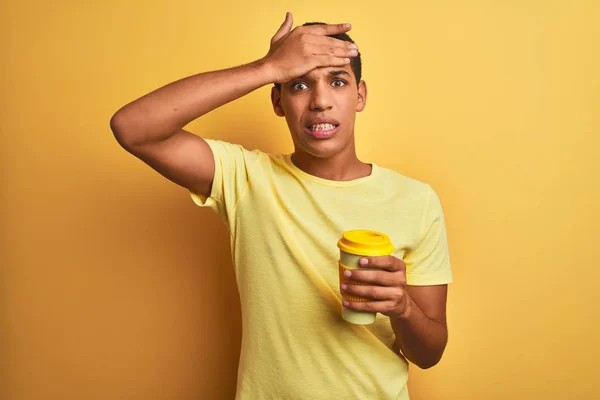 Young handsome arab man drinking take away coffee over isolated yellow background stressed with hand on head, shocked with shame and surprise face, angry and frustrated. Fear and upset for mistake.