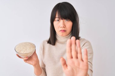 Genç güzel Çinli kadın ciddi ve kendinden emin ifade, savunma jesti ile durdurmak işareti yapıyor açık el ile izole beyaz arka plan üzerinde pirinç ile kase tutan