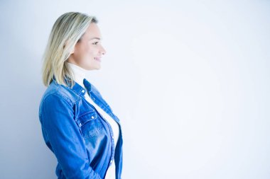 Denim gömlek giyen genç güzel kadın yan bakarak izole beyaz arka plan üzerinde duran, kendine güvenen gülümseme ile doğal yüz ile profil poz rahatlayın.