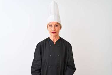 Orta yaş şef kadın yüzünde ciddi ifade ile izole beyaz arka plan üzerinde duran üniforma ve şapka giyiyor. Kameraya basit ve doğal bir bakış.