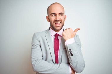 İzole arka plan üzerinde takım elbise ve mor kravat giyen genç iş adamı mutlu yüz görünümlü gülümseyerek ve başparmak ile yan işaret.