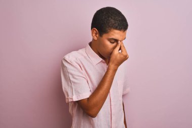 Genç yakışıklı Arap adam izole pembe arka plan yorgun sürtünme burun ve gözler üzerinde duran rahat gömlek giyen yorgunluk ve baş ağrısı hissi. Stres ve hayal kırıklığı kavramı.