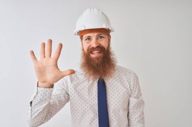Genç kızıl İrlandalı mimar adam izole beyaz arka plan üzerinde güvenlik kask giyen gösteren ve emin ve mutlu gülümserken parmakları ile beş işaret.