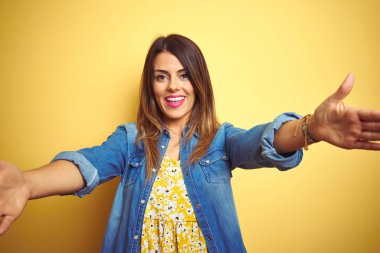 Genç güzel kadın sarı izole arka plan üzerinde duran sarılmak için açık kollarla gülümseyerek kameraya bakarak. Mutluluğu kucaklayan neşeli ifade.