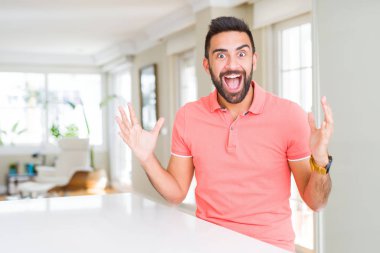 Yakışıklı İspanyol adam evde rahat t-shirt giyen deli kutluyor ve kollarını kaldırdı ve açık gözleri heyecan çığlık ile başarı için hayran. Kazanan kavramı