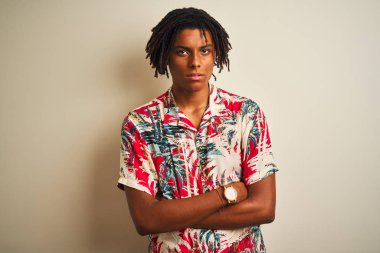 Izole beyaz arka plan şüpheci ve sinir üzerinde yazlık gömlek giyen tatilde dreadlocks ile Afro adam, çapraz kolları ile yüzünde ifade onaylamayan. Negatif kişi.