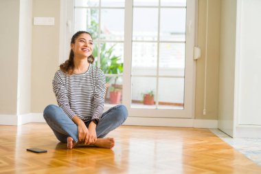 Ev uzak tarafına gülümseme ile yüzünde, doğal ifade arıyorum, yerde oturan genç güzel kadın. Kendine güvenen gülüyor.
