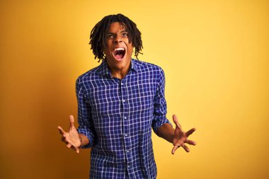 Yalnız sarı arka plan deli ve deli bağırarak ve agresif ifade ve kollar kaldırdı ile bağırıyor ayakta rahat gömlek giyen dreadlocks ile Afro adam. Hayal kırıklığı kavramı.