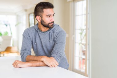 Yakışıklı İspanyol adam evde yan bakarak rahat sweatshirt giyen, kendine güvenen gülümseme ile doğal yüzü ile profil poz rahat.