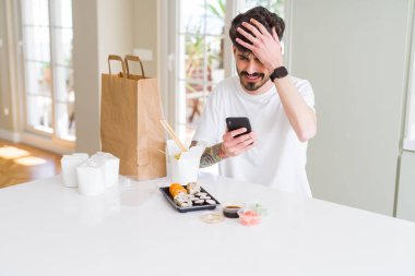 Eve teslim asya suşi yiyen ve akıllı telefon uygulaması kullanarak gıda sipariş genç adam baş el ile vurguladı, utanç ve sürpriz yüz ile şok, kızgın ve sinirli. Korku ve hata için üzgün.