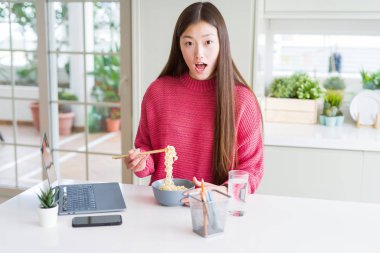 Güzel Asyalı kadın dizüstü bilgisayar kullanarak çalışan ve sürpriz bir yüz ile şok korkmuş asya erişte yeme, korku ifade korku ve heyecanlı