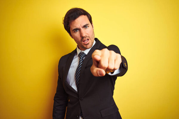 Young handsome businessman wearing suit and tie standing over isolated yellow background pointing displeased and frustrated to the camera, angry and furious with you