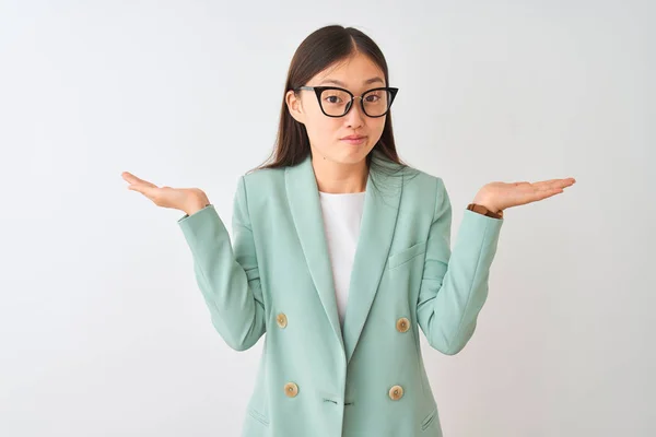 Chinese businesswoman wearing elegant jacket and glasses over isolated white background clueless and confused expression with arms and hands raised. Doubt concept.