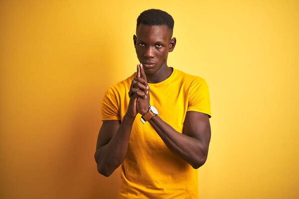 Young african american man wearing casual t-shirt standing over isolated yellow background Holding symbolic gun with hand gesture, playing killing shooting weapons, angry face