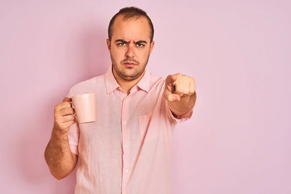 カメラとあなたに指で指を指して孤立したピンクの背景の上に立ってコーヒーのカップを飲む若い男は 手のサイン 正面から肯定的で自信のあるジェスチャー — ストック写真