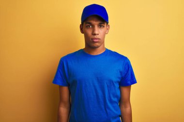 Genç yakışıklı Arap teslimat adam izole sarı arka plan üzerinde duran yüzünde ciddi ifade ile rahat. Kameraya basit ve doğal bir bakış.