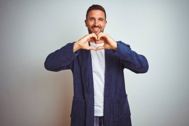 Rahat pijama ve cüppe giyen genç adam sabah izole arka plan üzerinde sevgi kalp sembolü ve elleriyle şekil gösteren gülümseyerek. Romantik kavram.