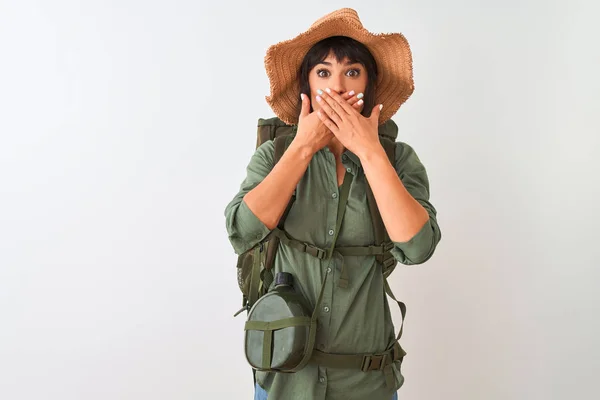 Hiker woman wearing backpack hat and water canteen over isolated white background shocked covering mouth with hands for mistake. Secret concept.