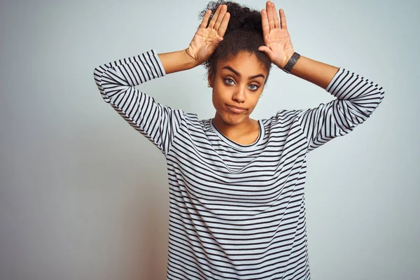 African american woman wearing navy striped t-shirt standing over isolated white background Doing bunny ears gesture with hands palms looking cynical and skeptical. Easter rabbit concept.