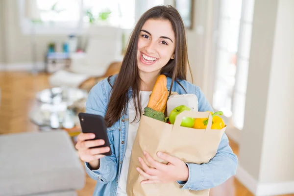 Mujer joven sosteniendo una bolsa de papel llena de alimentos frescos y usin —  Fotos de Stock