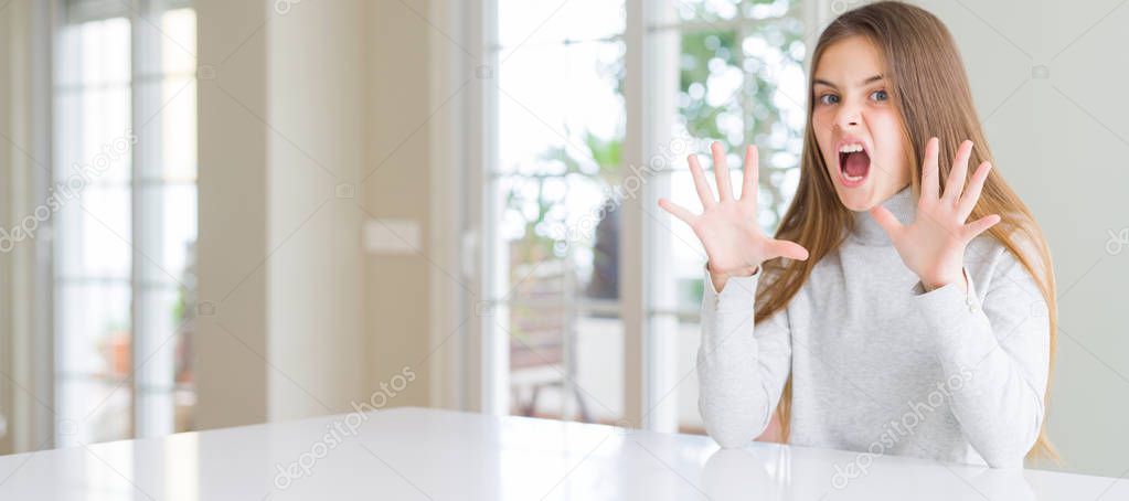 Wide angle picture of beautiful young girl kid wearing casual sweater afraid and terrified with fear expression stop gesture with hands, shouting in shock. Panic concept.