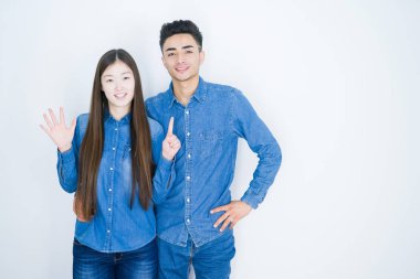 Beyaz izole arka plan üzerinde güzel genç asya çift gösteren ve parmakları ile işaret ederken emin ve mutlu gülümseyerek altı numara.