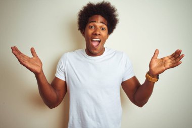 Afro saçlı afro saçlı adam izole beyaz arka plan üzerinde duran t-shirt giyen çok mutlu ve heyecanlı, kazanan ifade büyük bir gülümseme ile çığlık zafer kutluyor ve ellerini kaldırdı