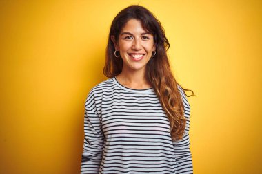 Genç güzel kadın yüzünde mutlu ve serin bir gülümseme ile yelllow izole arka plan üzerinde duran çizgili t-shirt giyiyor. Şanslı kişi.