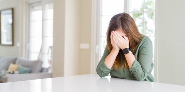 Güzel genç kadın evde üzgün ifadesi ile ağlarken elleriyle yüzünü kapatıyor. Depresyon kavramı.