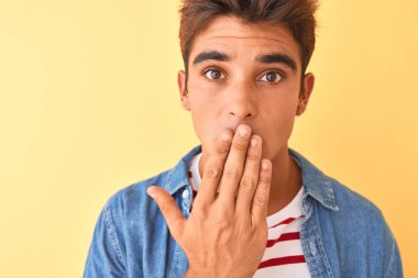 Genç yakışıklı adam izole sarı arka plan kapağı ağız üzerinde çizgili t-shirt ve denim gömlek giyen el hata için utanç ile şok, korku ifadesi, sessizlik, gizli kavram korkmuş