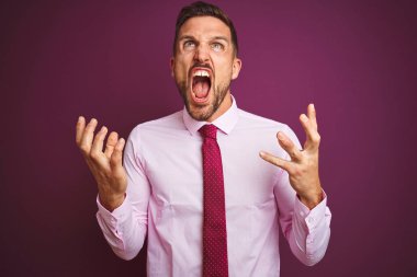 Genç iş adamı mor izole arka plan deli ve deli bağırarak üzerinde zarif gömlek ve kravat giyen ve agresif ifade ve kollar kaldırdı ile bağırıyor. Hayal kırıklığı kavramı.