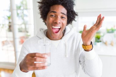 Afrika kökenli Amerikalı adam bir bardak su evde çok mutlu ve heyecanlı, kazanan ifade ile büyük çığlık zaferini kutluyor içme gülümse ve el kaldırdı