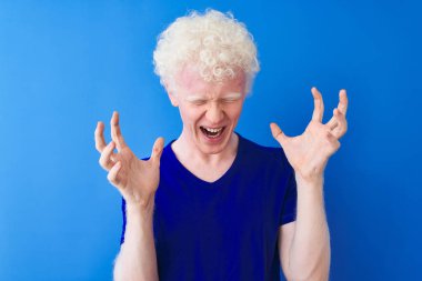 Genç albino sarışın adam rahat t-shirt izole mavi arka plan üzerinde ayakta giyen deli ve deli silah kaldırdı ve kapalı gözleri ile başarı için heyecan çığlık kutluyor. Kazanan kavramı