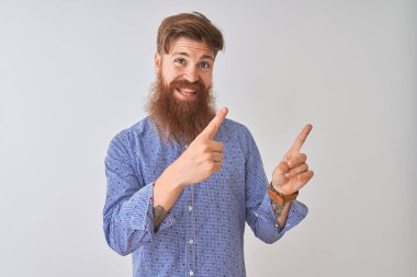 Genç kızıl İrlandalı adam izole beyaz arka plan üzerinde gülümseyerek ayakta rahat gömlek giyen ve yan iki el ve parmakları ile işaret kamera bakarak.