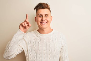 Genç yakışıklı adam başarılı bir fikir ile parmak işaret izole beyaz arka plan üzerinde duran kış kazak giyiyor. Çıktı ve mutlu. Bir numara.