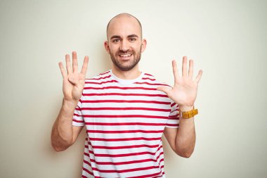 Sakallı genç kel adam beyaz izole arka plan üzerinde rahat çizgili kırmızı t-shirt giyen gösteren ve emin ve mutlu gülümserken parmakları sayısı dokuz ile işaret.