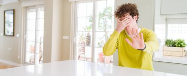 Evde genç yakışıklı adamın geniş açılı çekimi gözleri elleriyle kaplayıp hüzünlü ve korku ifadeyle dur jesti yapıyor. Utanmış ve olumsuz kavram.