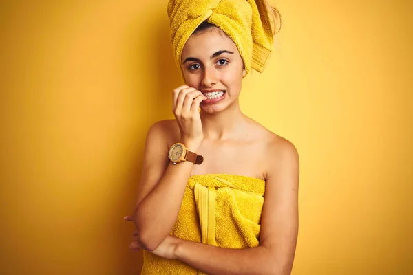 Young beautiful woman wearing a shower towel after bath over yellow isolated background looking stressed and nervous with hands on mouth biting nails. Anxiety problem.