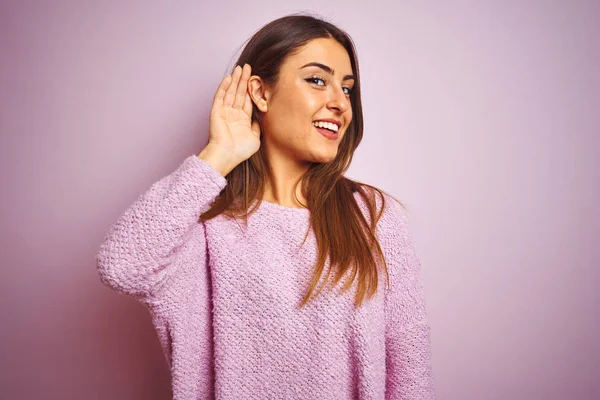 カジュアルなセーターを着た若い美しい女性は 噂やゴシップに耳を傾けて耳を上に微笑んで孤立したピンクの背景の上に立っています 聴覚障害の概念 — ストック写真