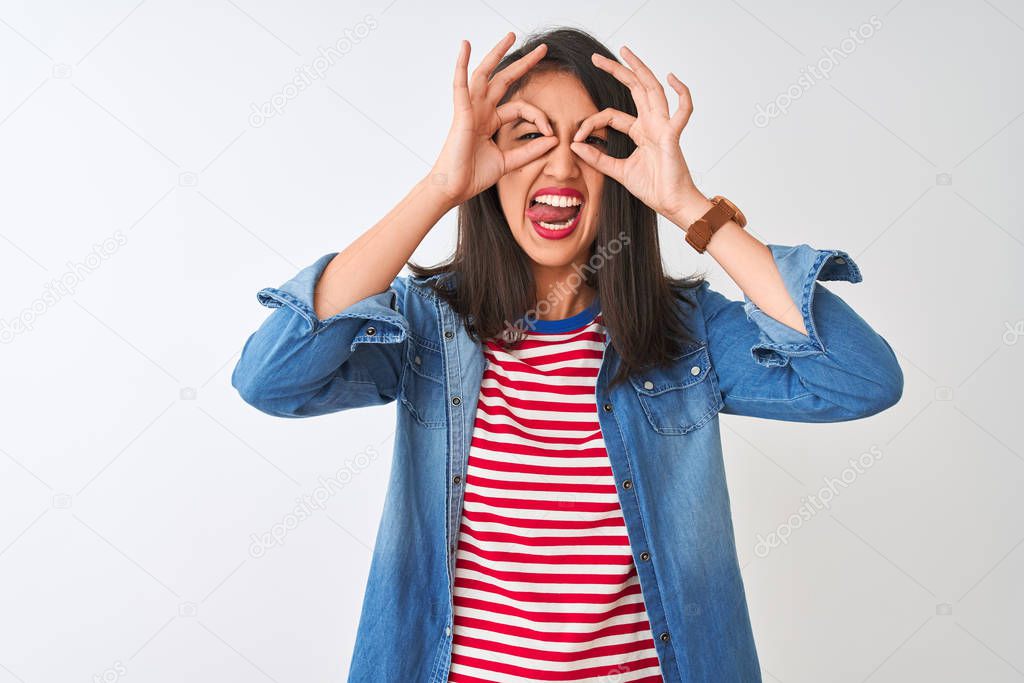 Young chinese woman wearing striped t-shirt and denim shirt over isolated white background doing ok gesture like binoculars sticking tongue out, eyes looking through fingers. Crazy expression.