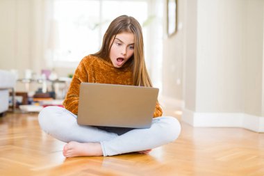 Evde dizüstü bilgisayar kullanarak eğitim alan güzel genç kız şaşkınlık içinde korkmuş, korku ve korku ifadesi ile heyecanlı