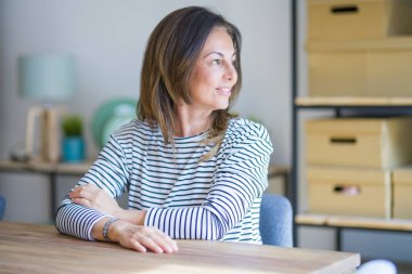 Orta yaş yaşlı kadın evde masaya oturan yan bakarak, kendine güvenen gülümseme ile doğal yüzü ile profil poz dinlenmek.