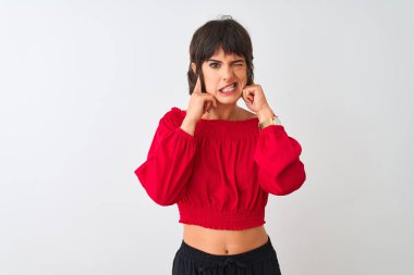 Genç güzel kadın kırmızı yaz t-shirt yüksek sesle gürültü için rahatsız ifade ile parmakları ile kulakları kapsayan izole beyaz arka plan üzerinde duran giyiyor. Sağır kavramı.