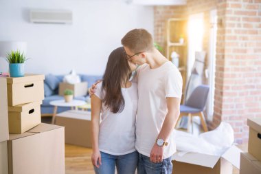 Genç güzel çift karton kutular etrafında yeni evde duran gözlük takarak öpüşme