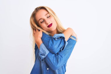 Yalnız beyaz arka plan üzerinde duran rahat kot gömlek giyen genç güzel kadın kendini mutlu ve olumlu sarılma, kendinden emin gülümseyen. Öz sevgi ve öz bakım