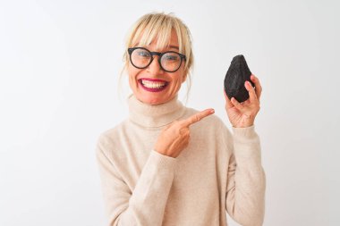 Orta yaş kadın izole beyaz arka plan üzerinde avokado tutan gözlük takan çok mutlu el ve parmak ile işaret