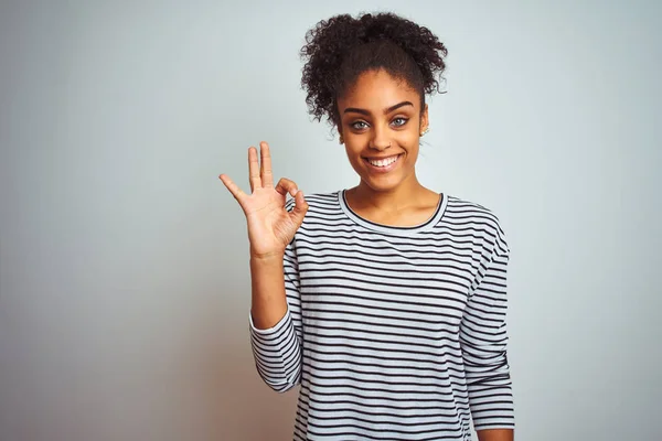 African american woman wearing navy striped t-shirt standing over isolated white background smiling positive doing ok sign with hand and fingers. Successful expression.